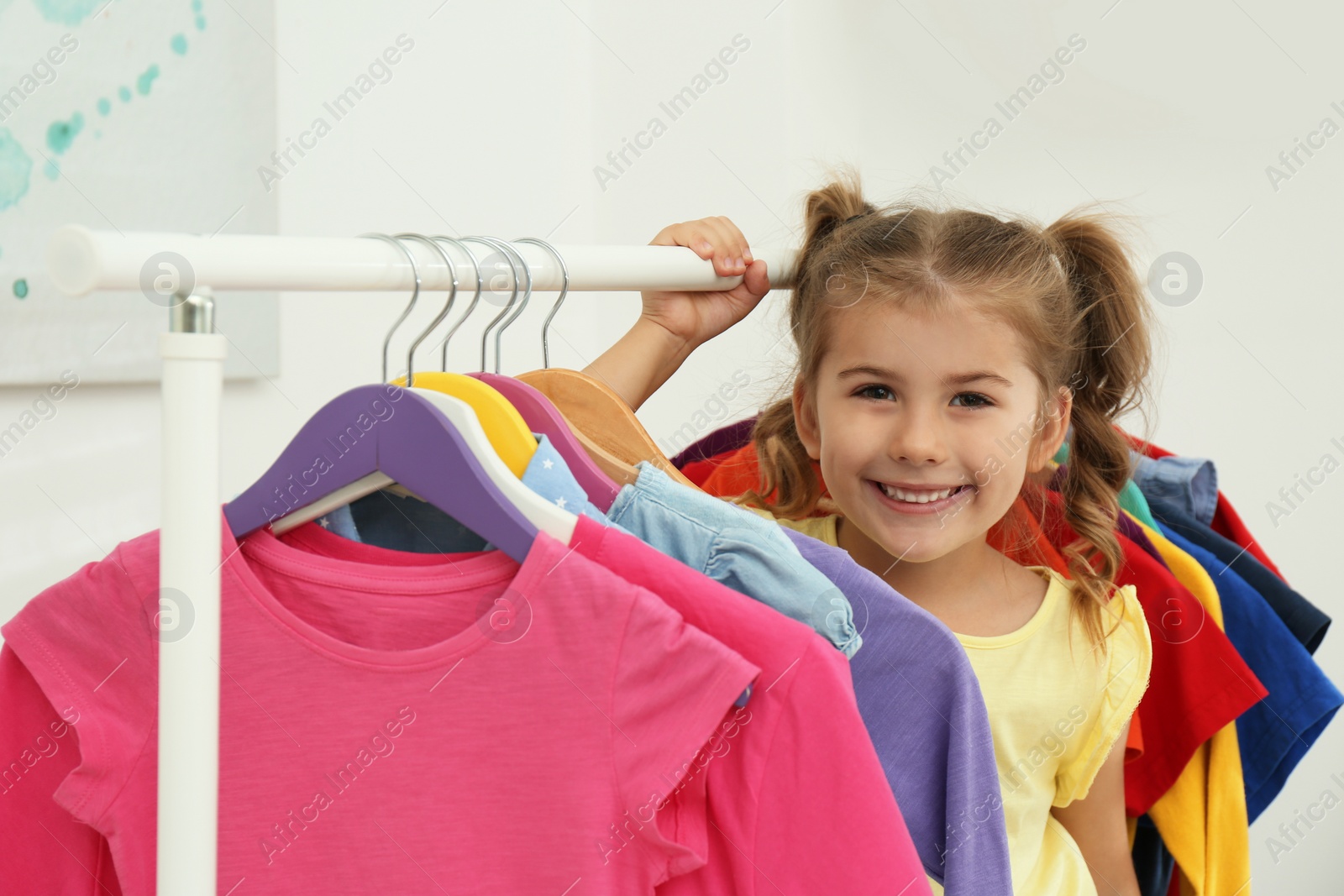 Photo of Little girl choosing clothes on rack indoors