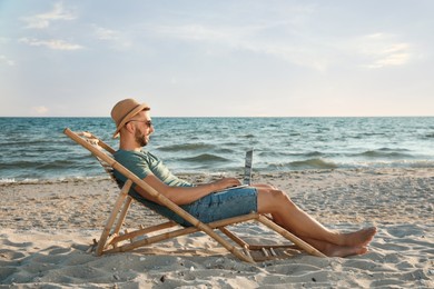 Photo of Man working with laptop in deck chair on beach