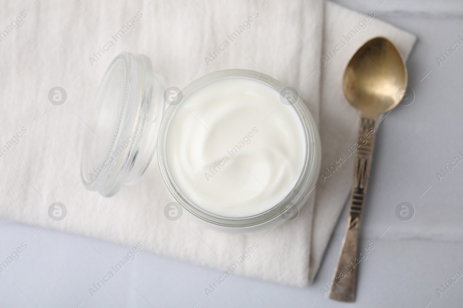 Photo of Delicious natural yogurt in glass jar and spoon on white table, top view