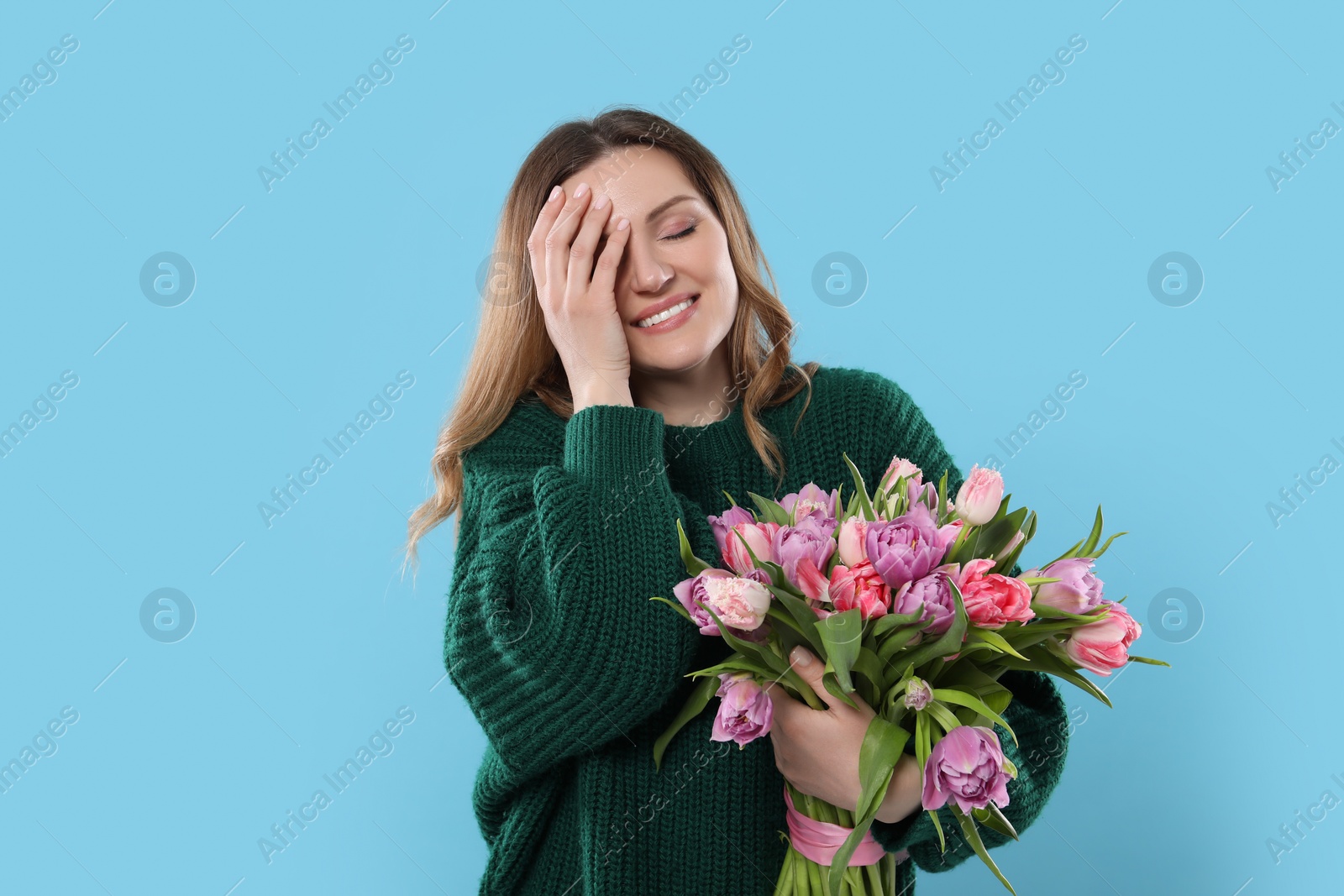 Photo of Happy young woman with bouquet of beautiful tulips on light blue background