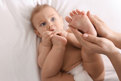 Photo of Mother massaging her cute baby with oil on bed, closeup