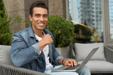 Portrait of handsome young African-American man with laptop in outdoor cafe