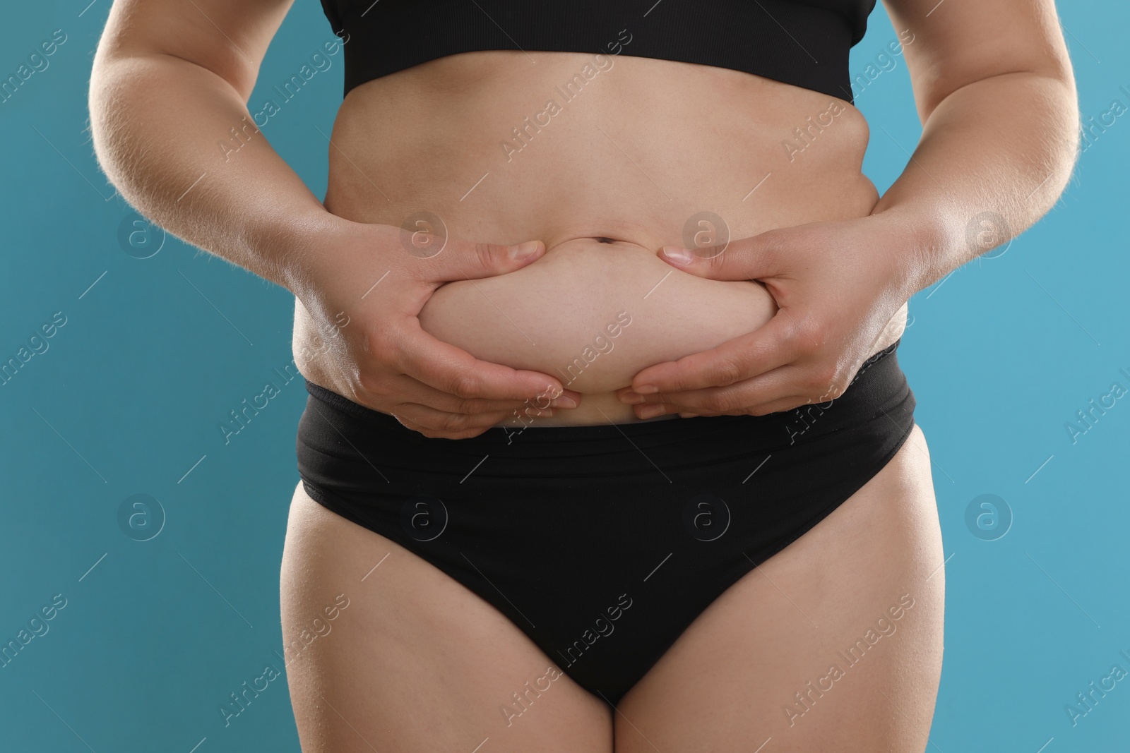 Photo of Woman touching belly fat on light blue background, closeup. Overweight problem