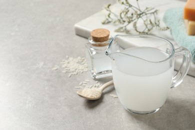 Photo of Glass jug with natural rice water and grains on light grey table. Space for text