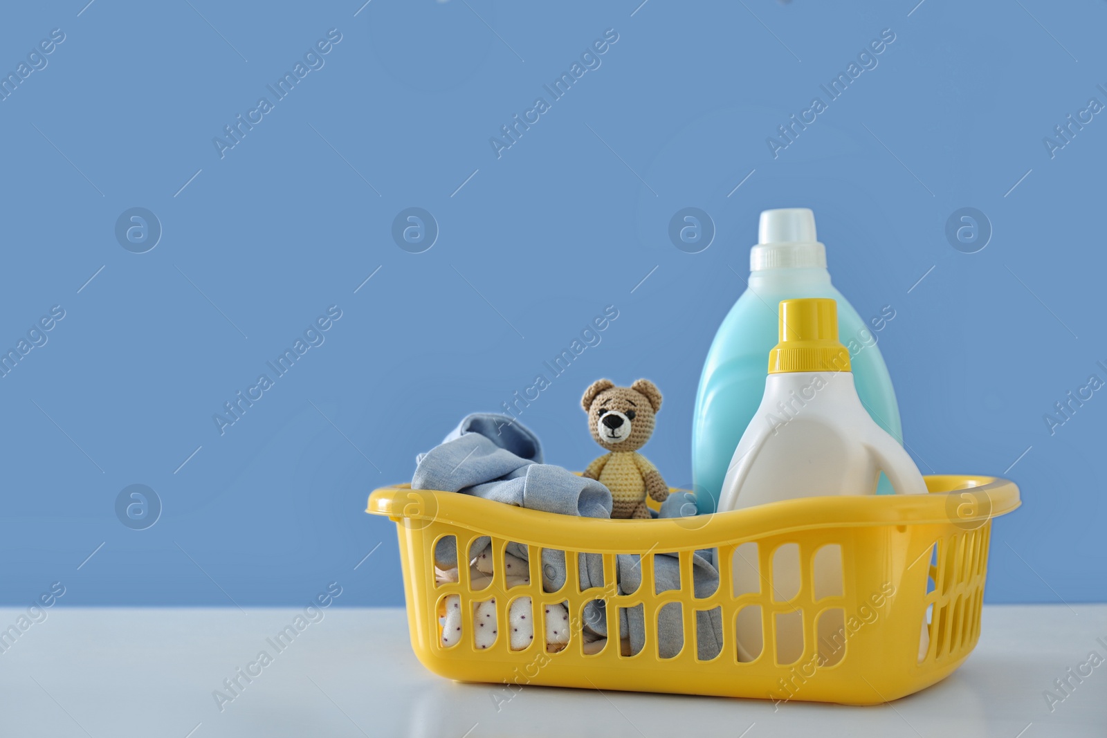 Photo of Detergents and children's clothes on white table near blue wall