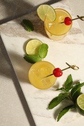 Photo of Glassestasty pineapple cocktail decorated with cherry and lime on light grey marble table, top view