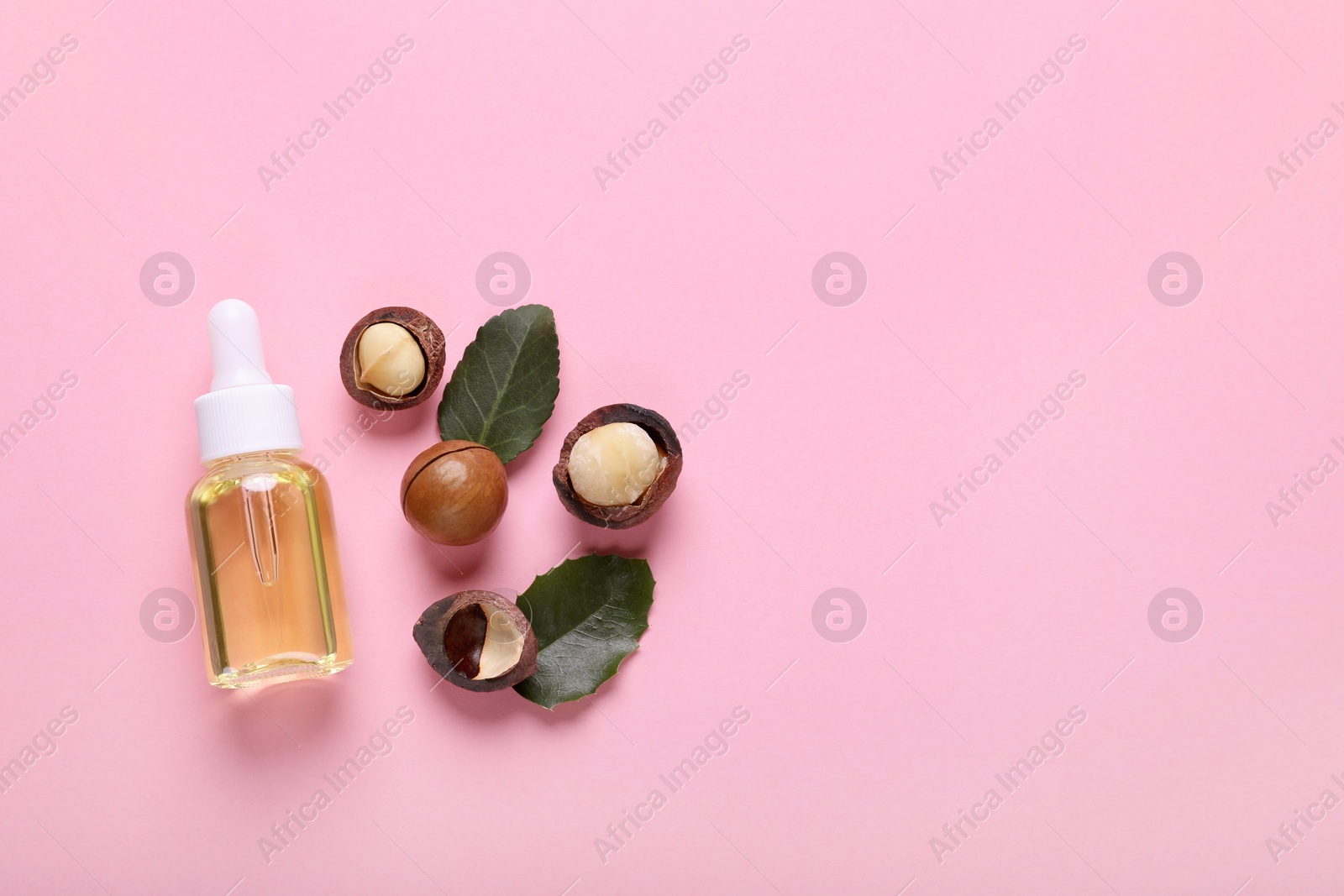 Photo of Delicious organic Macadamia nuts, natural oil and green leaves on pink background, flat lay. Space for text