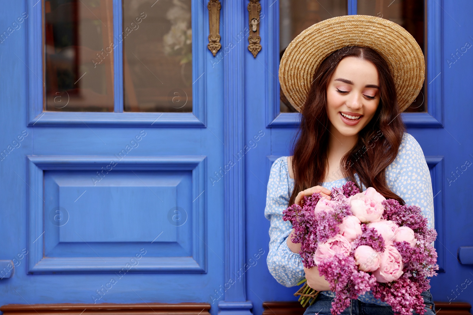 Photo of Beautiful woman with bouquet of spring flowers near blue wooden doors, space for text