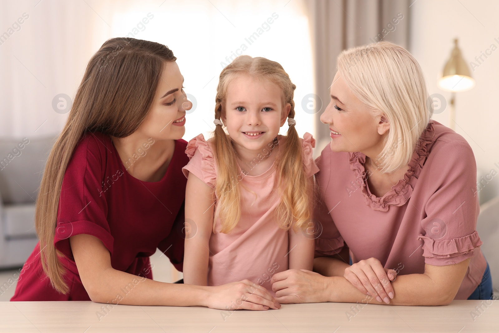 Photo of Portrait of young woman, her mature mother and daughter at table indoors