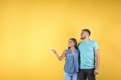 Photo of Young couple with air conditioner remote on color background, copy space text
