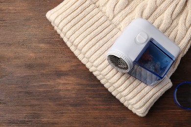 Photo of Modern fabric shaver and white knitted hat on wooden table, top view. Space for text