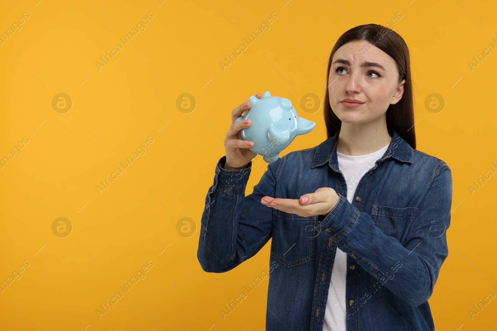 Photo of Sad woman with piggy bank on orange background, space for text