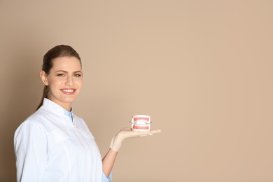 Photo of Female dentist holding jaws model on color background. Space for text