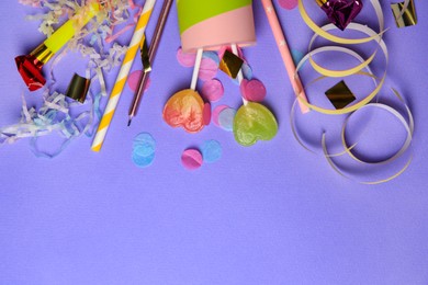 Party popper, lollipops and festive decor on violet background, flat lay