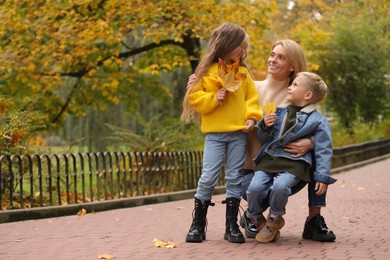 Happy mother and her children with dry leaves in autumn park