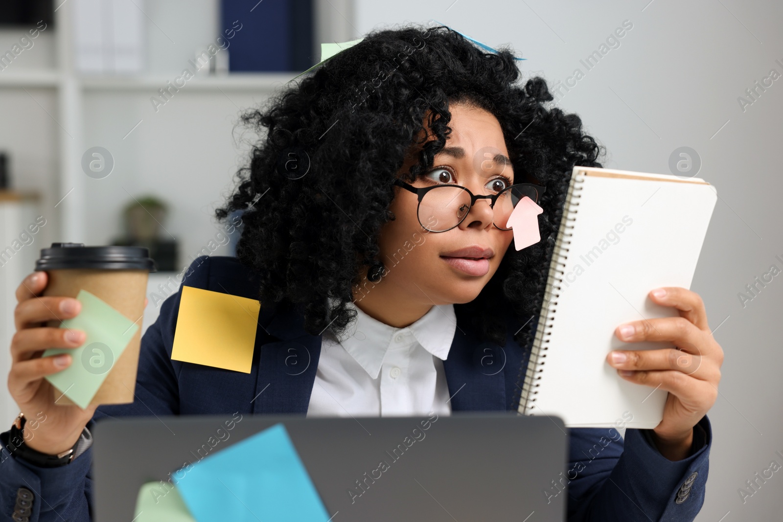 Photo of Deadline concept. Stressed woman looking at notepad and holding paper cup in office. Many sticky notes everywhere as reminders