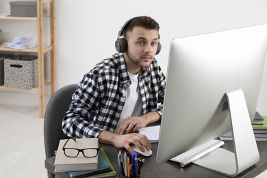 Photo of Young man in headphones using modern computer for studying at home. Distance learning