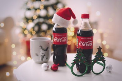 MYKOLAIV, UKRAINE - January 01, 2021: Bottles of Coca-Cola, cup and party glasses on table against blurred Christmas lights