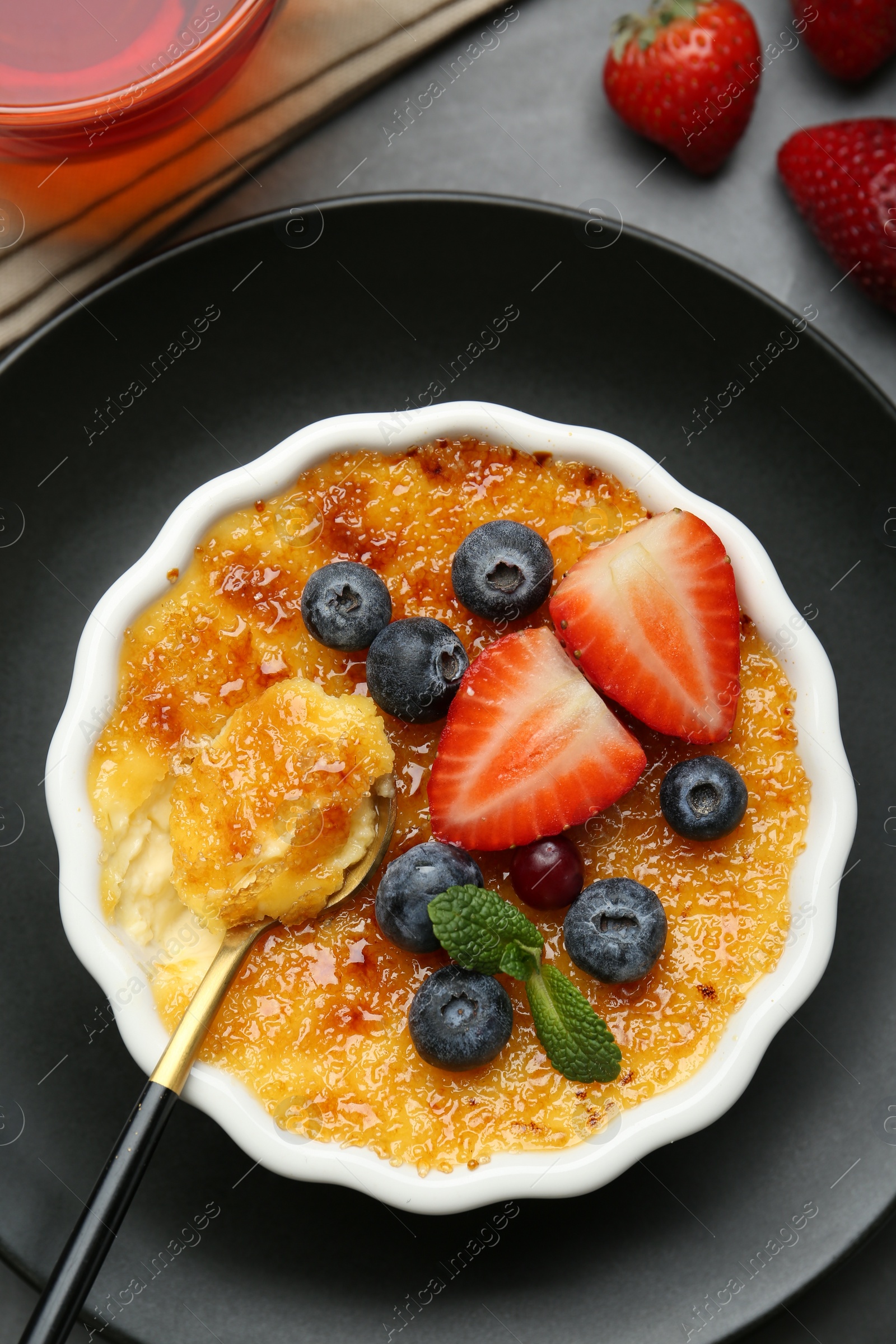 Photo of Delicious creme brulee with berries and mint in bowl served on grey table, flat lay