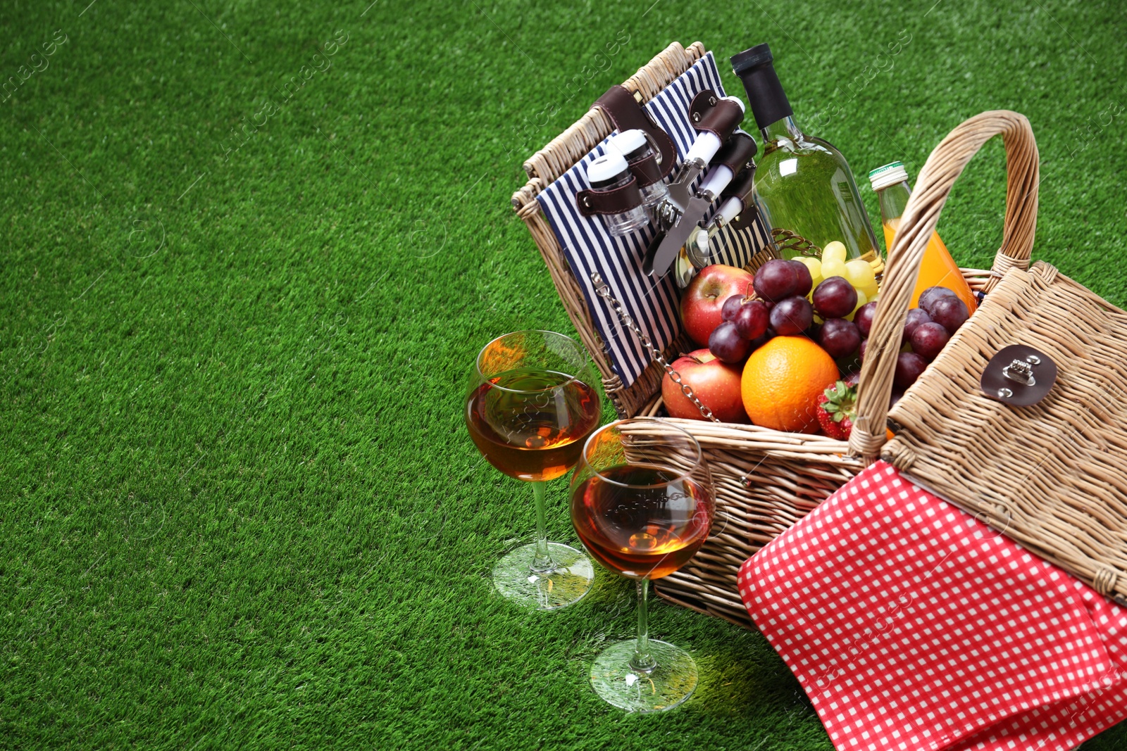 Photo of Wicker picnic basket with different products on green grass, space for text