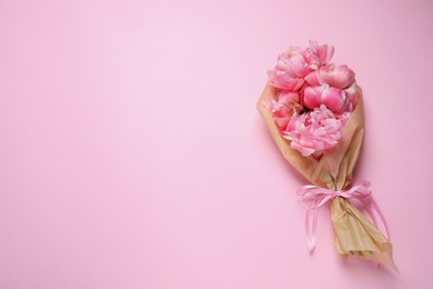 Photo of Beautiful bouquet of peonies wrapped in paper on pink background, top view. Space for text