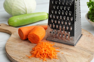 Photo of Grater and fresh ripe carrot on wooden board, closeup