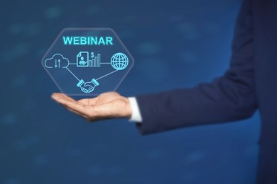 Image of Webinar. Businessman holding virtual scheme with icons on blue background, closeup
