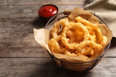 Photo of Homemade crunchy fried onion rings in wire basket on wooden background, closeup