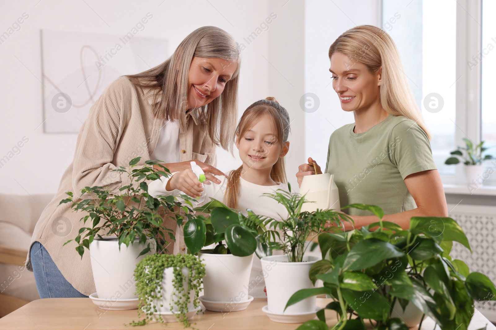 Photo of Three generations. Happy grandmother, her daughter and granddaughter watering houseplants at home