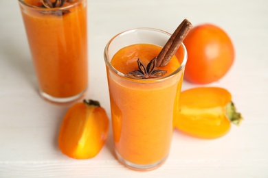 Photo of Tasty persimmon smoothie with anise and cinnamon on white wooden table, closeup