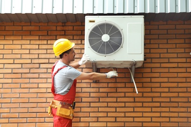 Photo of Male technician fixing air conditioner outdoors