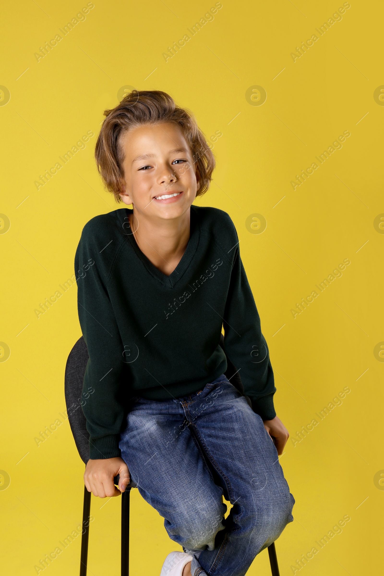 Photo of Cute little boy sitting in chair on yellow background