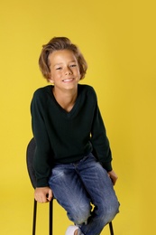 Photo of Cute little boy sitting in chair on yellow background