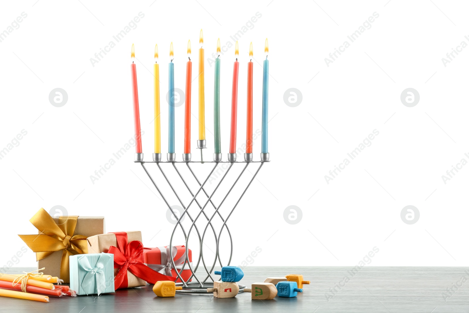 Photo of Hanukkah celebration. Menorah with colorful candles, dreidels and gift boxes on wooden table against white background