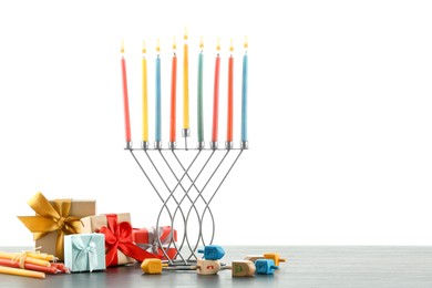 Photo of Hanukkah celebration. Menorah with colorful candles, dreidels and gift boxes on wooden table against white background