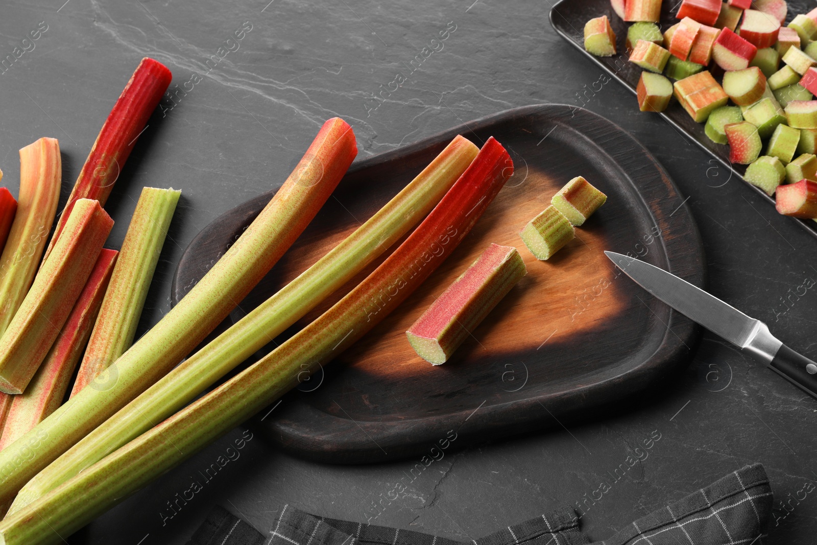 Photo of Whole and cut rhubarb stalks and knife on black table, flat lay