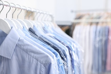 Photo of Dry-cleaning service. Many different clothes in plastic bags hanging on rack indoors, closeup