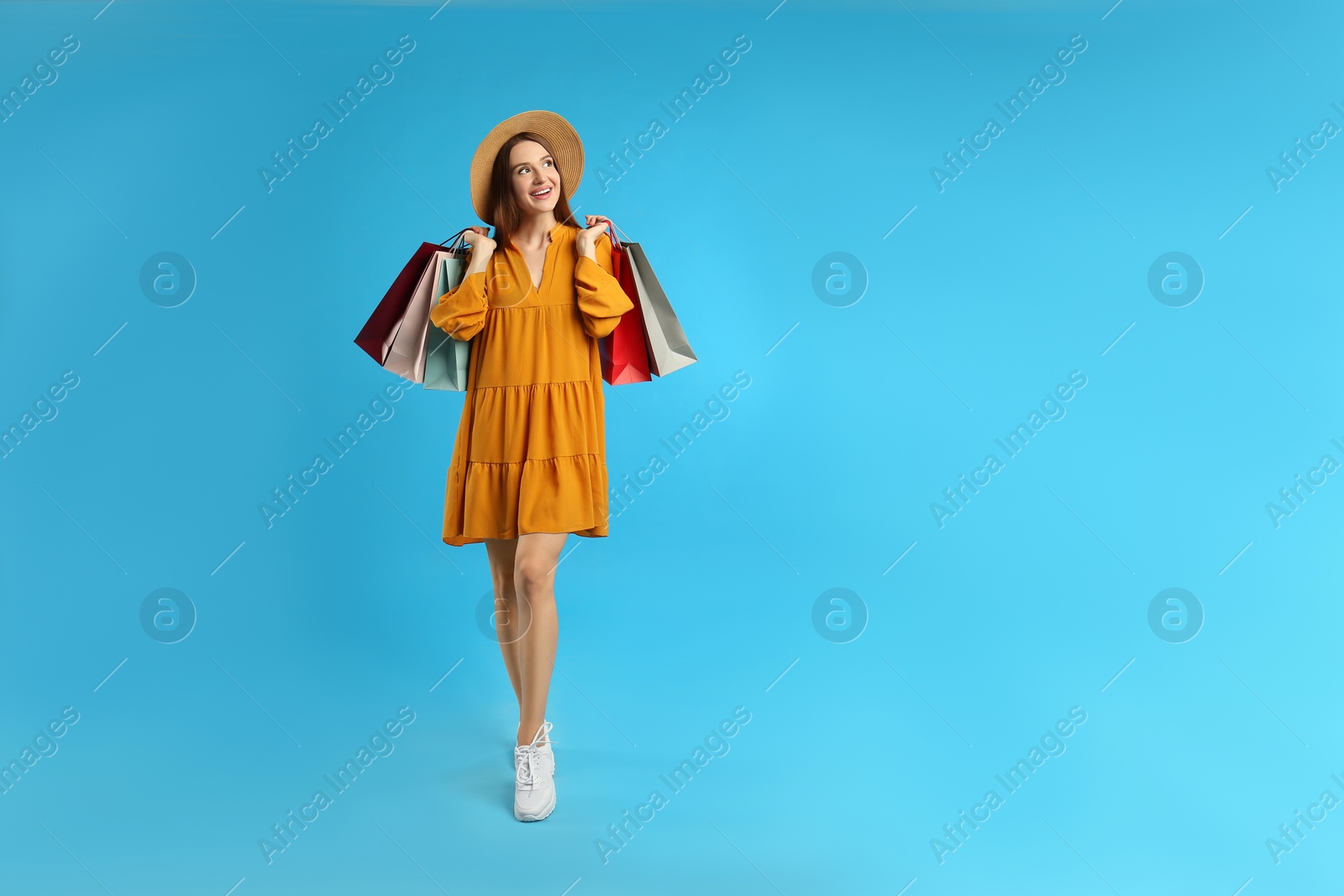 Photo of Beautiful young woman with paper shopping bags on light blue background