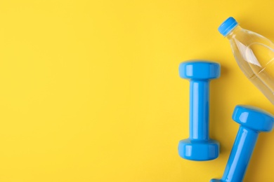 Photo of Vinyl dumbbells and bottle of water on color background, flat lay. Space for text