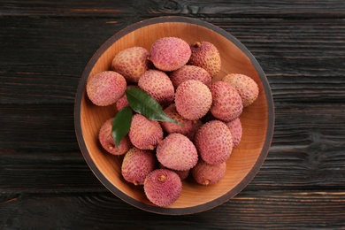 Photo of Fresh ripe lychee fruits in bowl on dark wooden table, top view