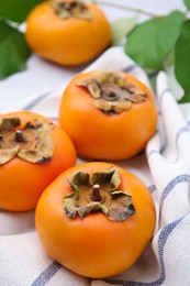 Photo of Delicious ripe juicy persimmons on striped cloth, closeup