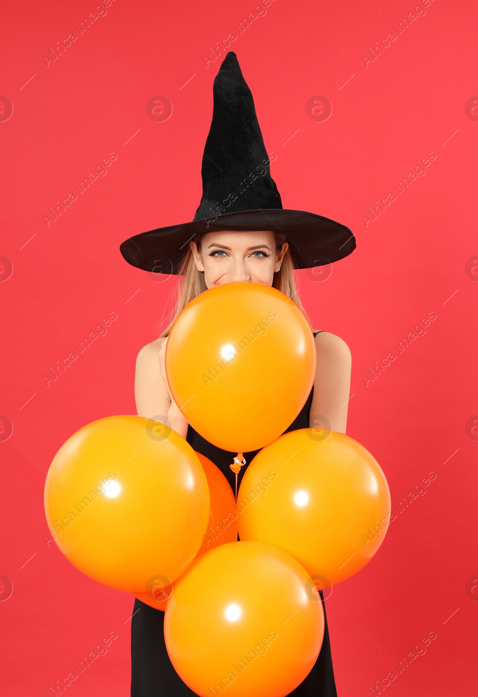 Photo of Beautiful woman wearing witch costume with balloons for Halloween party on red background