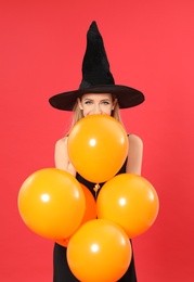 Photo of Beautiful woman wearing witch costume with balloons for Halloween party on red background