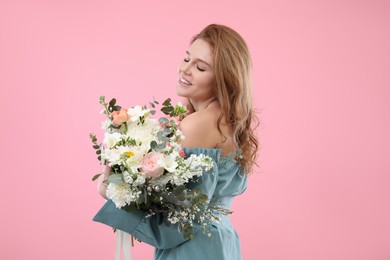 Beautiful woman with bouquet of flowers on pink background