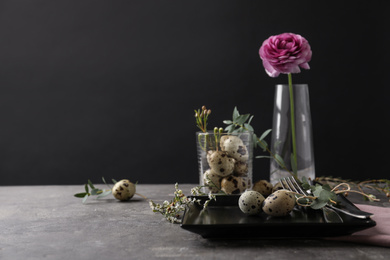 Festive Easter table setting with quail eggs and floral decoration on dark background. Space for text