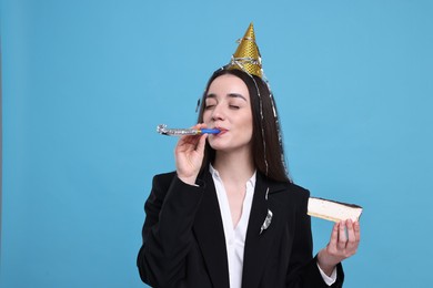 Woman in party hat with blower and piece of tasty cake on light blue background