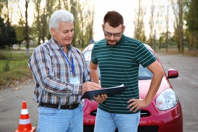 Senior instructor with clipboard and man outdoors. Get driving license