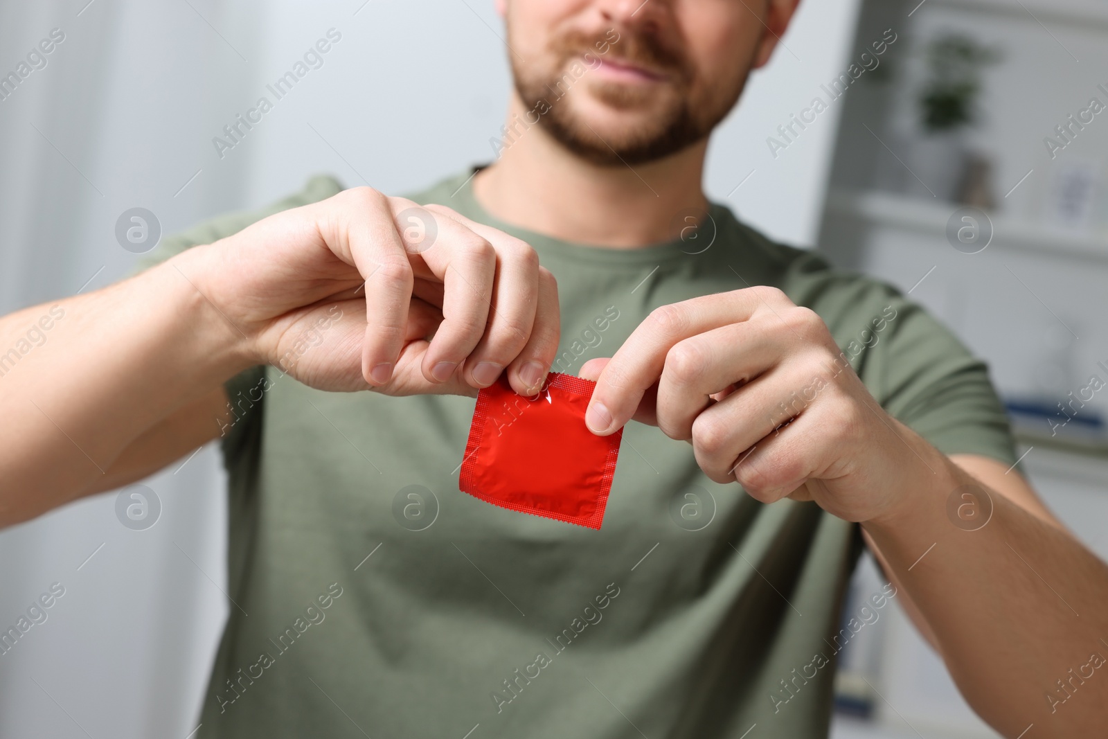 Photo of Closeup view of man opening pack with condom indoors