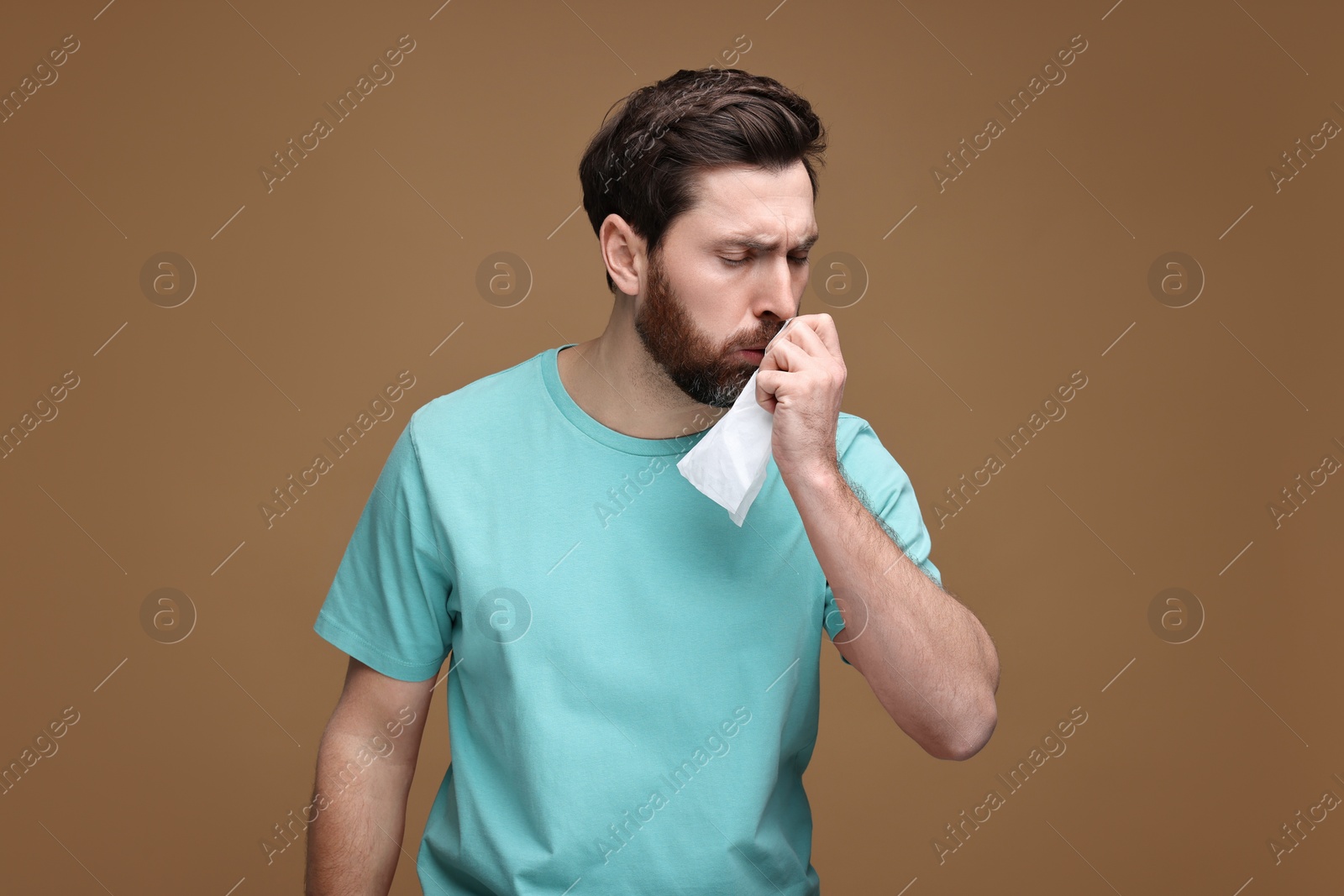 Photo of Sick man with tissue coughing on brown background