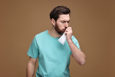 Sick man with tissue coughing on brown background